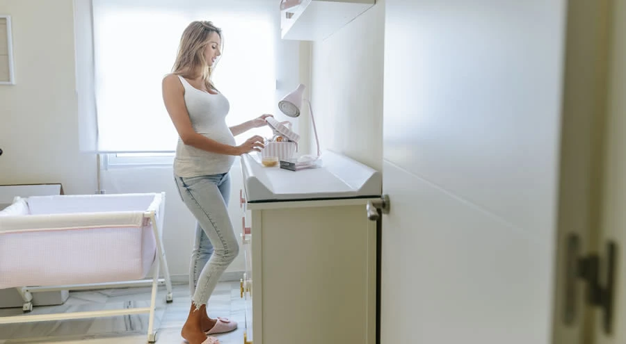 Trudna zena stoji u decijoj sobi pokraj kreveca i podloge za presvlacenje beba.